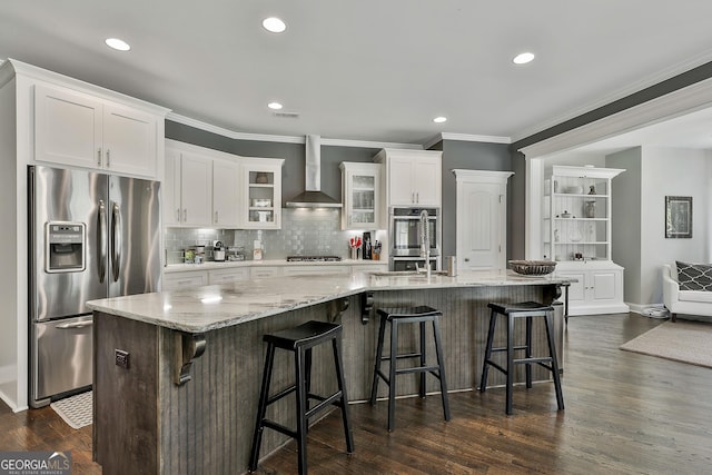 kitchen with appliances with stainless steel finishes, wall chimney exhaust hood, ornamental molding, tasteful backsplash, and white cabinetry