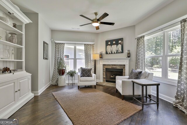 living room featuring healthy amount of natural light, a stone fireplace, a ceiling fan, and baseboards