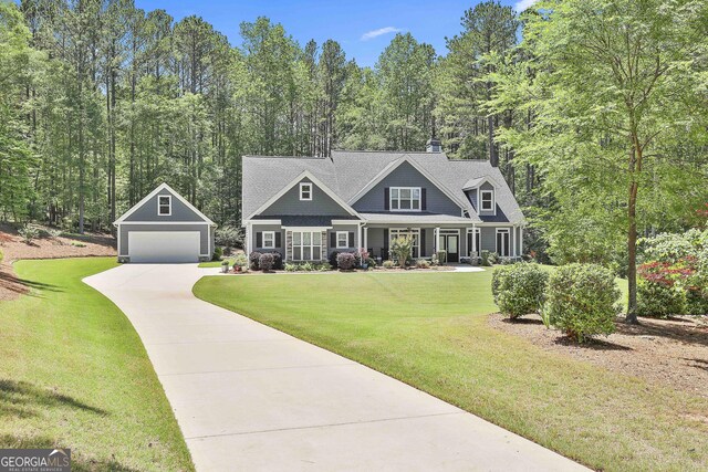 view of front of property with an outdoor structure, a detached garage, a front yard, covered porch, and driveway