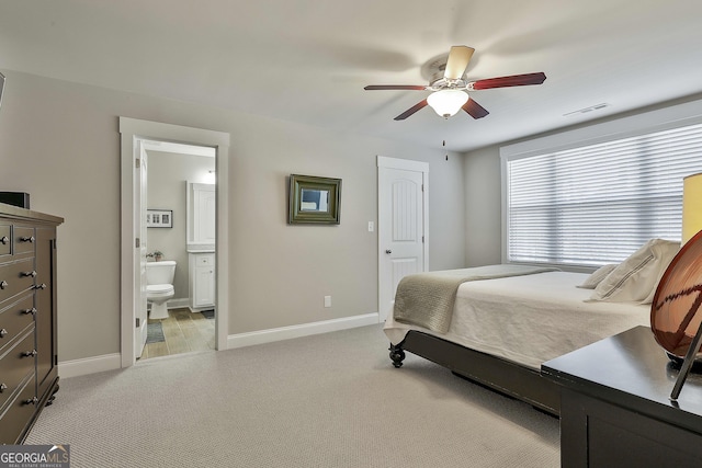bedroom featuring light carpet, baseboards, ceiling fan, and ensuite bathroom
