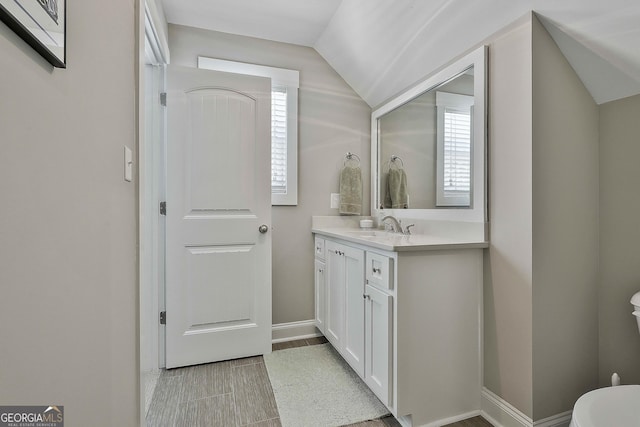 bathroom featuring toilet, vanity, lofted ceiling, and baseboards