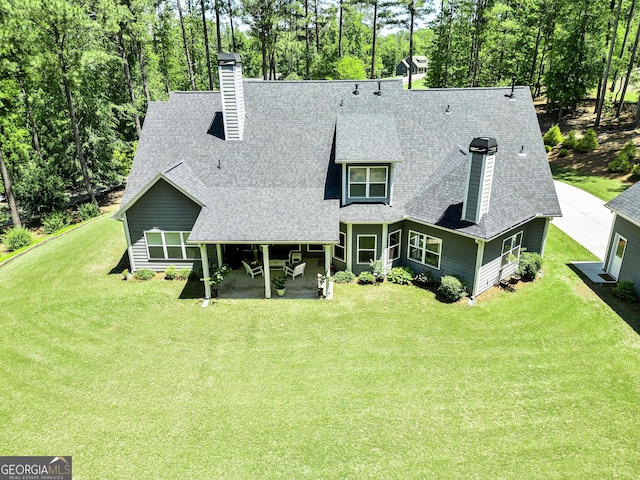 rear view of property with roof with shingles, a lawn, and a chimney