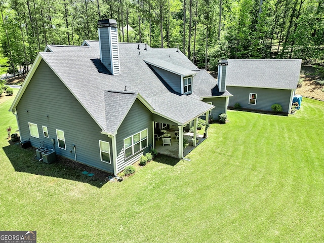 back of house with a chimney, roof with shingles, a lawn, and cooling unit