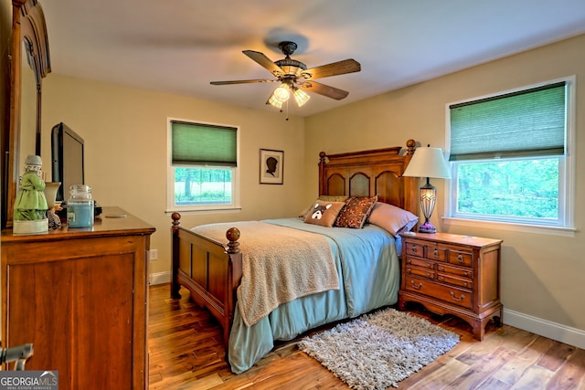 bedroom with multiple windows, light wood finished floors, and baseboards
