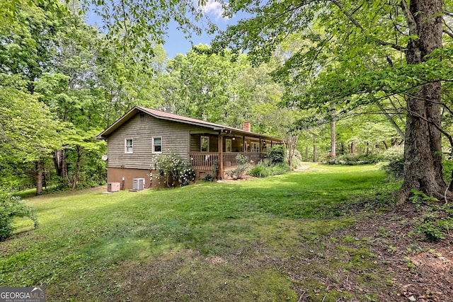 view of side of property featuring a chimney, a lawn, and central AC