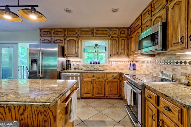 kitchen featuring appliances with stainless steel finishes, light tile patterned floors, brown cabinetry, backsplash, and a sink