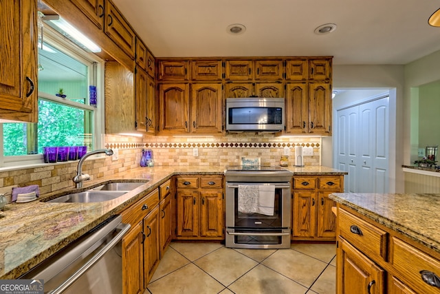 kitchen featuring stainless steel appliances, a sink, light tile patterned floors, brown cabinetry, and tasteful backsplash