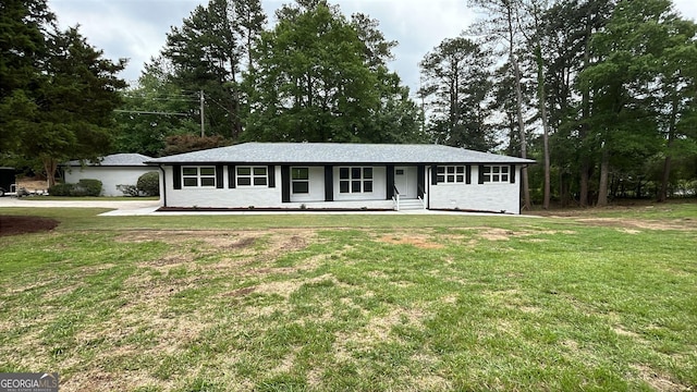 ranch-style house with a front yard, view of wooded area, and a porch