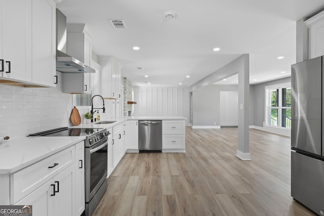 2604 Flat Shoals Rd SW, Conyers, GA 30094 - kitchen featuring stainless steel appliances, wall chimney exhaust hood, a sink, a peninsula, and light wood-type flooring