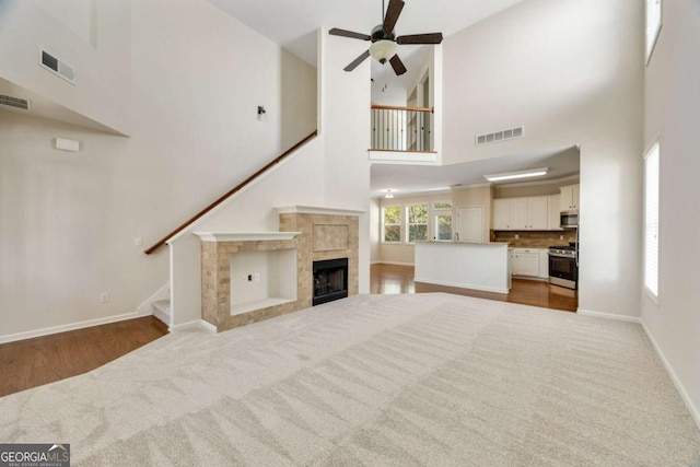 unfurnished living room featuring a ceiling fan, a towering ceiling, stairway, carpet, and a tile fireplace