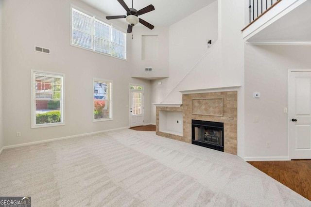 unfurnished living room featuring a high ceiling, a ceiling fan, baseboards, a tiled fireplace, and carpet flooring