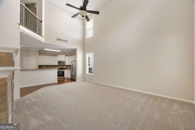 unfurnished living room with ceiling fan, carpet floors, baseboards, and a towering ceiling