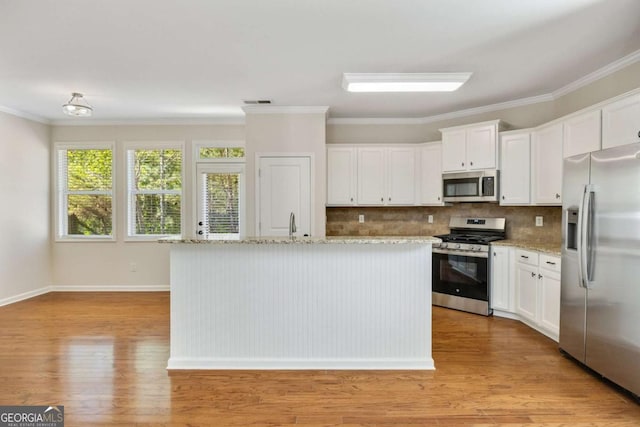 kitchen with appliances with stainless steel finishes, light wood-style floors, tasteful backsplash, white cabinets, and ornamental molding