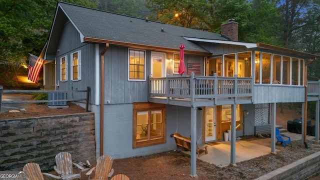 rear view of property featuring a patio, a sunroom, central air condition unit, a chimney, and a shingled roof