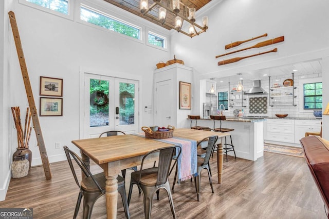 dining room featuring wooden ceiling, wood finished floors, a towering ceiling, a chandelier, and french doors
