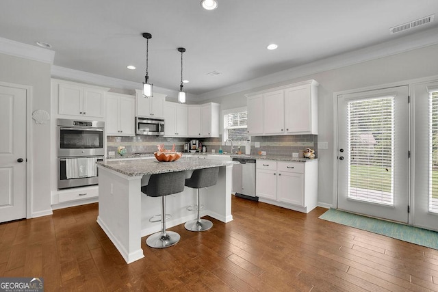 4050 Pleasant Woods Dr, Cumming, GA 30028 - kitchen with stainless steel appliances, crown molding, white cabinets, a center island, and tasteful backsplash