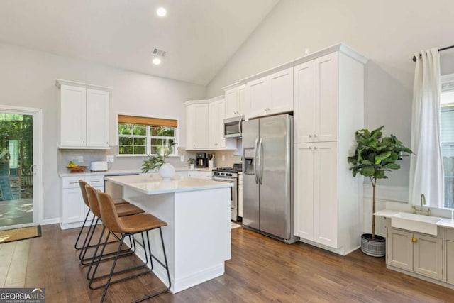 kitchen featuring appliances with stainless steel finishes, a sink, light countertops, a breakfast bar area, and a center island
