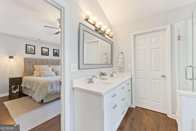 ensuite bathroom with tiled shower, wood finished floors, a ceiling fan, vaulted ceiling, and double vanity