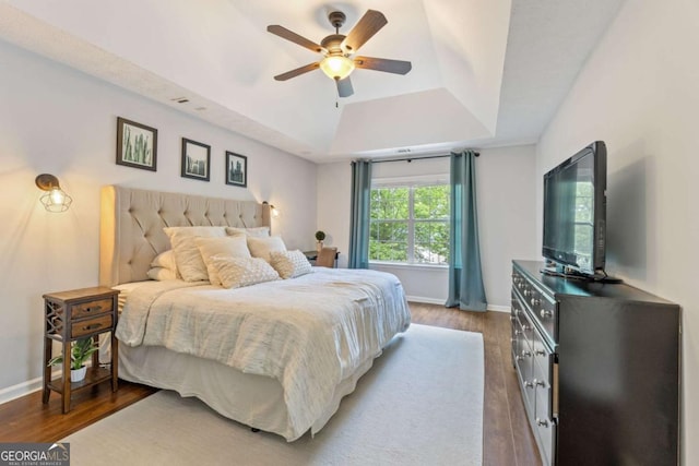 bedroom with a tray ceiling, wood finished floors, baseboards, and a ceiling fan