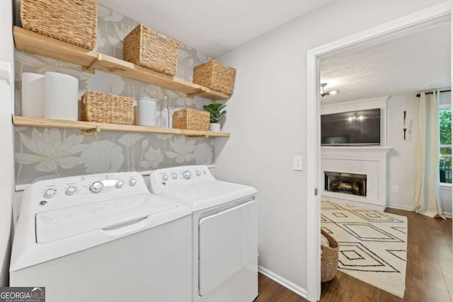 clothes washing area featuring washer and clothes dryer, dark wood-style flooring, baseboards, a fireplace, and a textured ceiling