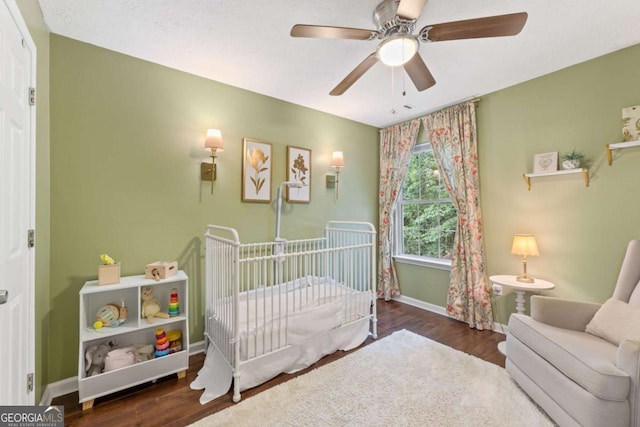 bedroom featuring a nursery area, baseboards, wood finished floors, and a ceiling fan