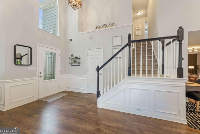 entrance foyer featuring stairs, wainscoting, wood finished floors, a decorative wall, and a high ceiling