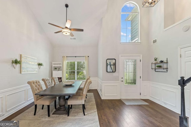 dining space featuring high vaulted ceiling, wood finished floors, a decorative wall, ceiling fan, and wainscoting