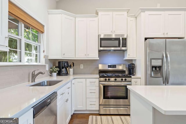 kitchen with appliances with stainless steel finishes, a sink, light countertops, backsplash, and white cabinets