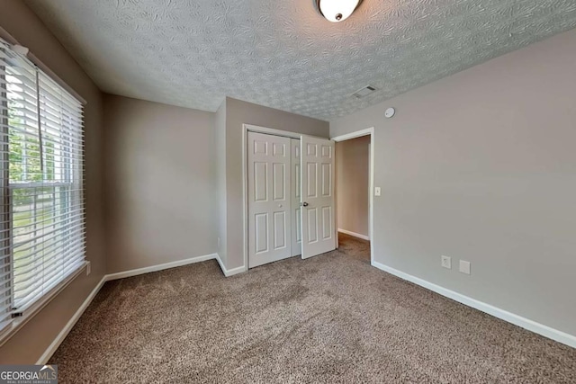 unfurnished bedroom with carpet flooring, a closet, baseboards, and a textured ceiling