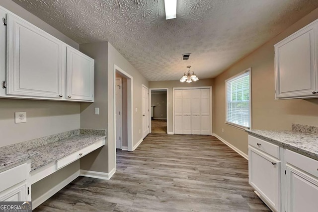 unfurnished dining area with a chandelier, light wood-style flooring, baseboards, and a textured ceiling