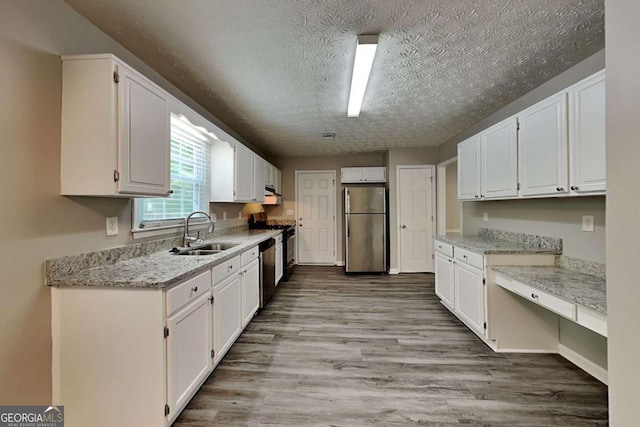 kitchen with stainless steel appliances, a sink, white cabinetry, a textured ceiling, and wood finished floors