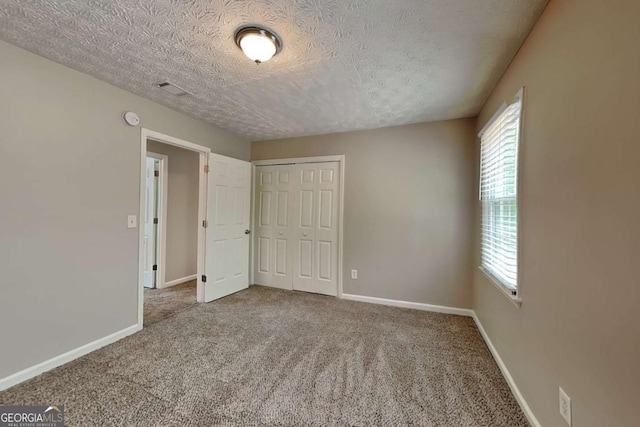 unfurnished bedroom featuring multiple windows, a textured ceiling, carpet, and a closet