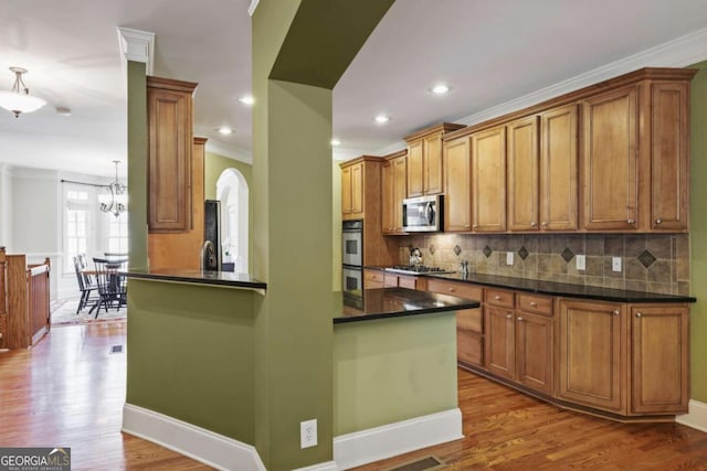kitchen with appliances with stainless steel finishes, dark countertops, brown cabinetry, backsplash, and crown molding
