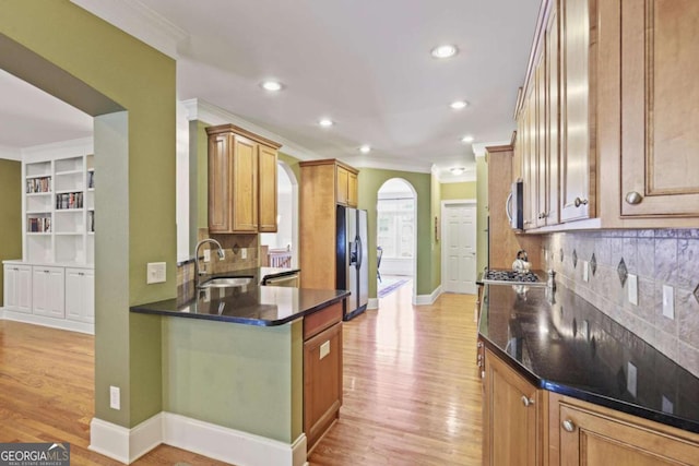 kitchen featuring a sink, crown molding, appliances with stainless steel finishes, light wood-type flooring, and decorative backsplash