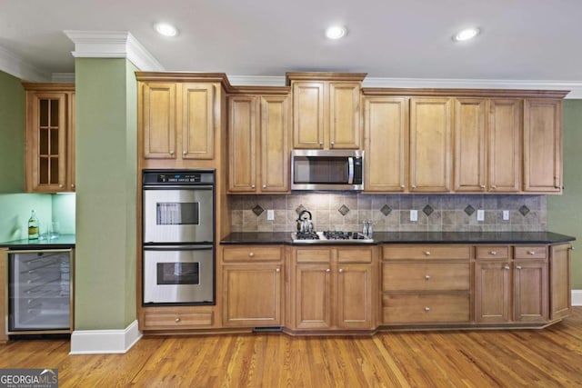 kitchen with appliances with stainless steel finishes, beverage cooler, ornamental molding, light wood-style flooring, and baseboards