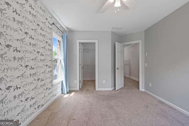 unfurnished bedroom featuring carpet, a walk in closet, baseboards, and ceiling fan