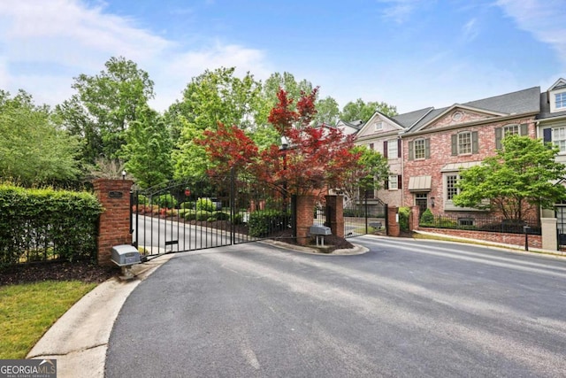 view of asphalt street with a gated entry, a gate, and curbs