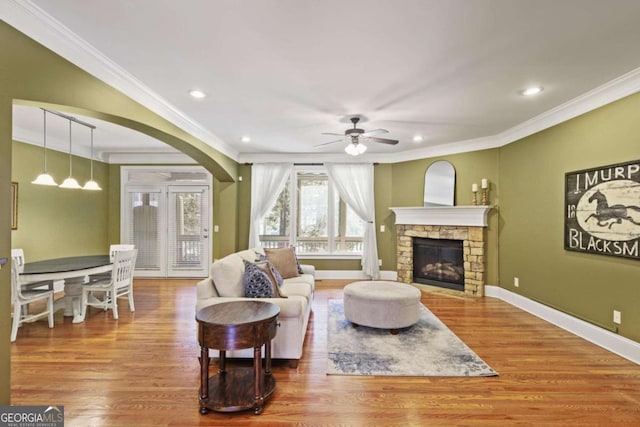 living room with ornamental molding, ceiling fan, wood finished floors, a stone fireplace, and recessed lighting