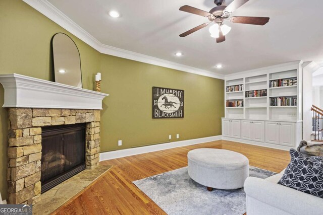 living area with crown molding, a ceiling fan, a stone fireplace, wood finished floors, and recessed lighting