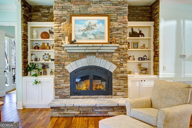 living area with wood finished floors, a stone fireplace, and built in features