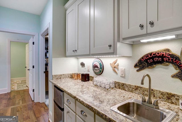 kitchen with a sink, wood finished floors, light stone countertops, and baseboards