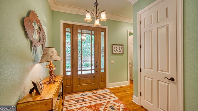 foyer featuring ornamental molding, light wood-style flooring, a chandelier, and baseboards