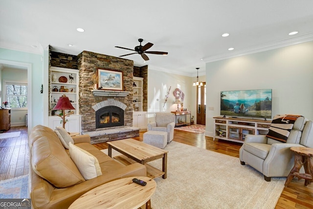 living room with wood finished floors, crown molding, ceiling fan, a stone fireplace, and recessed lighting