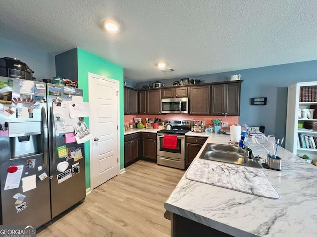 kitchen featuring stainless steel appliances, dark brown cabinetry, light countertops, light wood-style flooring, and a textured ceiling