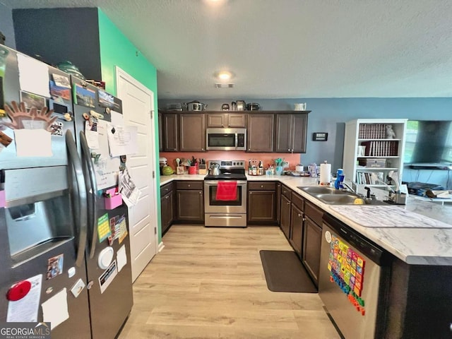 kitchen featuring stainless steel appliances, a sink, light wood-style floors, dark brown cabinets, and light countertops