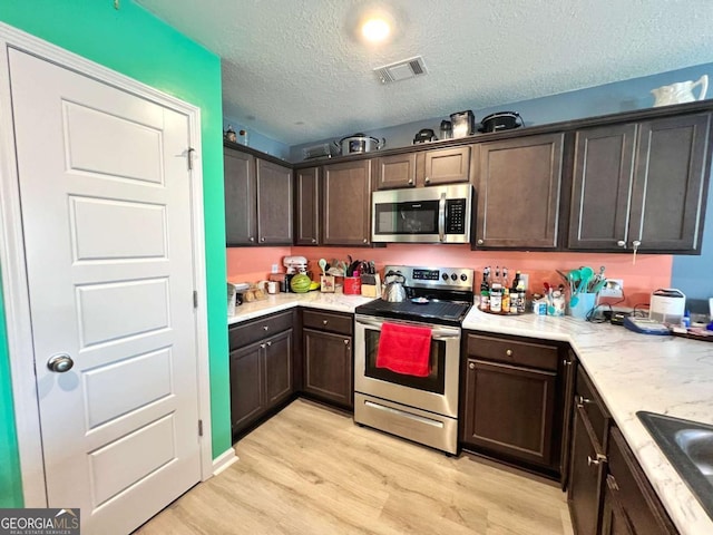 kitchen with appliances with stainless steel finishes, light wood-type flooring, dark brown cabinetry, a textured ceiling, and a sink