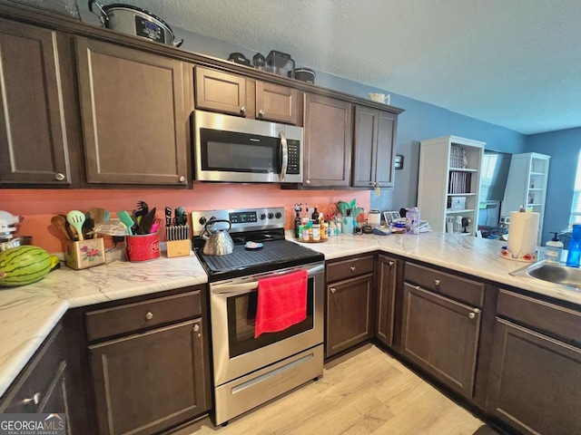 kitchen with appliances with stainless steel finishes, light wood finished floors, dark brown cabinets, and light countertops