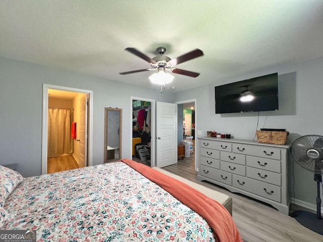 bedroom featuring wood finished floors, a walk in closet, a closet, ensuite bath, and a textured ceiling