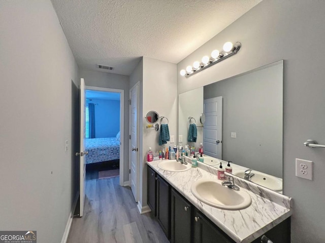 ensuite bathroom featuring wood finished floors, a textured ceiling, double vanity, and baseboards