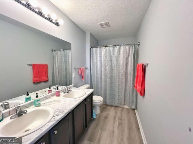 full bathroom with wood finished floors, a textured ceiling, double vanity, toilet, and baseboards